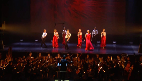 Dancers in red performing with an orchestra